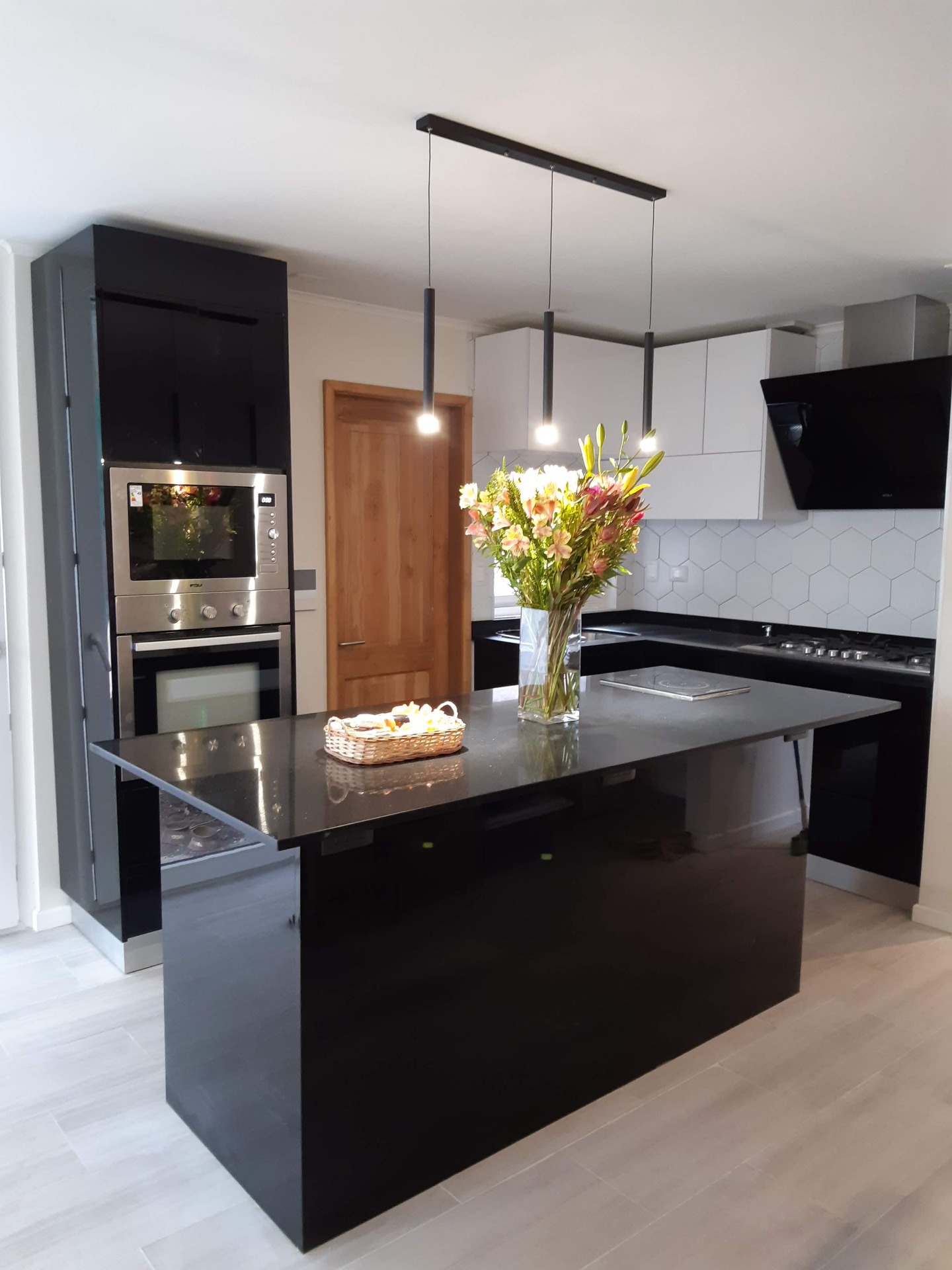 Cocina moderna con isla oscura, flores en jarrón, horno y campana negra, azulejos hexagonales blancos.